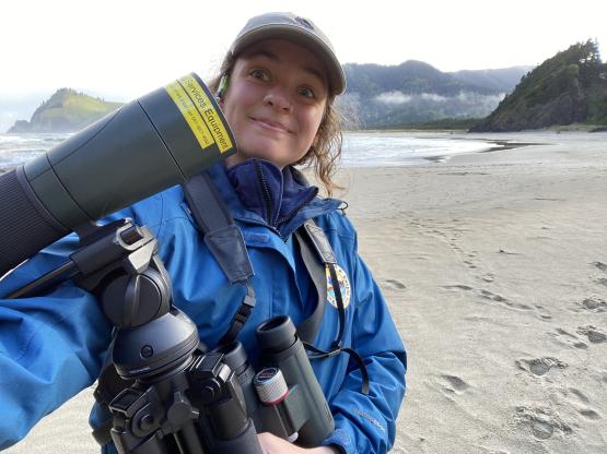 Lila Bowen looking happy on a beach in Oregon with a scope and her binoculars