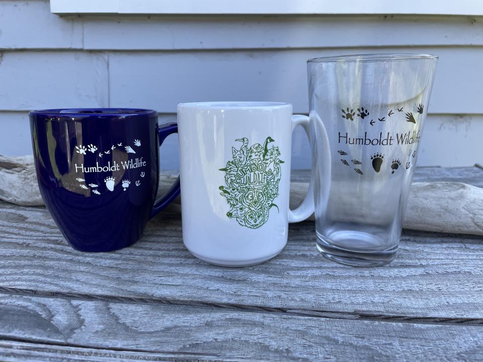 A blue mug, a white mug, and a pint glass with Wigss logos 